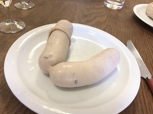 Zwei bayerische Weißwürste (eine davon halb nackt) ohne Senf auf einem Teller.